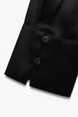 Camisa azul marino de satén con cuello solapa, escote en pico y mangas largas con puños abotonados.
