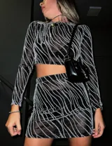 Conjunto de top manga larga y minifalda con estampado de líneas brillantes sobre tela transparente negra.