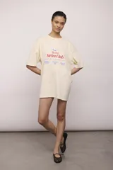 Remerón de manga corta color crema, corte oversize y cuello redondo. Estampado frontal con texto y un dibujo de una persona nadando, con la frase "The Peel Swim Club".