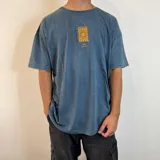Remera azul con efecto gastado, corte oversize y estampa trasera con un sol amarillo dentro de un cuadrado negro y texto "This is living" y "Sunsets sessions".