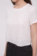 Remera blanca con calados formando flores, de corte crop y mangas cortas con dobladillo.