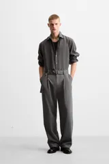 Pantalón negro de corte ancho con cinturón de tela con hebilla metálica y pliegues frontales.