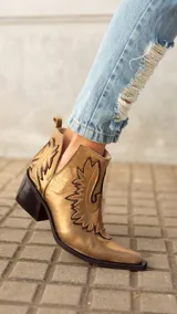 Botas cortas de cuero color bronce con bordados y recortes con motivos de estrellas.