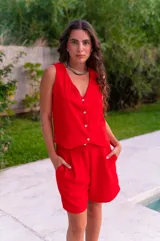 Conjunto de dos piezas color rojo vibrante, compuesto por un chaleco sin mangas con escote en V y botones frontales, y un short de tiro alto con pliegues y bolsillos laterales.