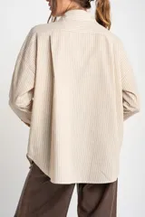 Camisa oversize a rayas verticales color beige y blanco, con cuello clásico, cierre frontal con botones, dos bolsillos de parche en el pecho y mangas largas con puños abotonados.