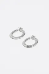 Caravanas de aro con diseño ovalado y acabado metálico plateado. Poseen un cuerpo tubular grueso, cierre de presión y detalle de grabado en uno de los laterales.