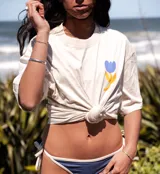 Remera oversize color crudo con estampado en la espalda de un paisaje tropical con palmeras, sol y mar en tonos amarillo, azul y celeste.