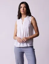 Blusa blanca de gasa marca Zac & Rachel, sin mangas, con cuello a la base con frunce, escote en V con botones, delantera plisada y apliques en crochet.