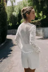 Top blanco de encaje con bordados florales, cuello redondo y mangas largas.