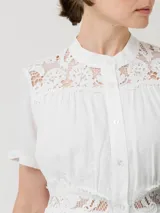 Vestido corto blanco de lino y viscosa, con cuello mao, mangas cortas, cierre frontal con botones, encaje en la parte superior y en la cintura, y forro a tono.