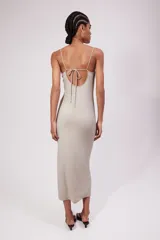 Vestido midi de punto suave color gris, con escote redondo profundo y espalda escotada. Modelo entallado con breteles spaghetti que se entrelazan en bucles y se atan en la espalda.