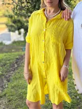 Vestido camisero corto de lino color amarillo, con cuello camisero, mangas cortas con botón, cierre frontal con botones y corte holgado.