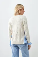 Sweater tejido color crema con diseño de trenzas, corte holgado y camisa celeste a rayas en los laterales.
