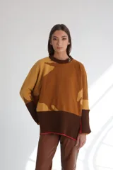 Sweater de punto color marrón con diseño abstracto en tonos mostaza y detalle de broche metálico en el cuello.