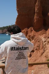 Buzo canguro con capucha, color blanco con estampado de camuflaje en tonos grises. Estampado en la espalda con el logo de la marca y nombres de ciudades.