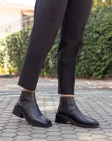 Botinetas de cuero negro con diseño de caña baja y puntera cuadrada. Presentan un panel trasero con textura tipo reptil y un taco bloque bajo de estilo moderno.