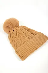 Gorro de lana color tostado con diseño trenzado y pompón de piel sintética en la parte superior.