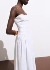 Vestido midi blanco sin mangas, con escote recto, detalle fruncido en los laterales y cierre de cremallera en la parte posterior.