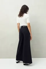 Pantalón de jean negro de corte ultra wide, tiro medio y detalles metálicos en la cintura.