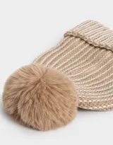 Gorro de lana tejido a crochet en color beige con detalles en blanco y pompón de piel sintética en la parte superior.