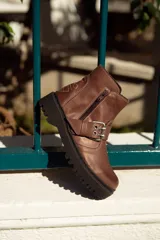 Bota corta color marrón de cuero, con hebilla metálica y cierre lateral.