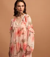 Vestido largo de chiffon con estampado floral en tonos rosados y beige. Tiene escote en V con lazo ajustable, mangas largas abullonadas con volados y forro interior.