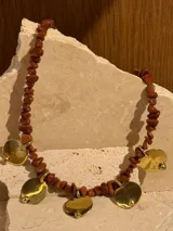 Collar corto con cuentas de piedras de colores y dijes de monedas de bronce. Collar largo con cadena dorada y dije de metal.