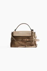 Cartera bandolera color visón, con correa ajustable y asa de mano. Presenta solapa con cierre magnético y trabilla decorativa con hebilla metálica.