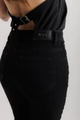 Pantalón de jean negro elastizado con corte ajustado y volados en la parte baja de la pierna. El ruedo es más largo en la parte trasera y tiene terminación descosida.