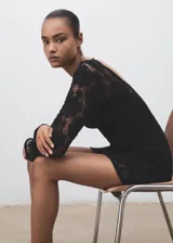 Vestido corto negro de tejido de crochet con manga larga acampanada y cuello redondo. Presenta un diseño con espalda abierta ajustada con lazo.