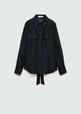 Camisa negra de lyocell y poliéster, con cuello camisero, dos bolsillos de solapa en el pecho, manga larga con puños abotonados y cierre frontal con botones. Diseño recto y cierre de lazo ajustable.