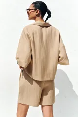 Camisa color beige de cuello solapa con escote pico y manga corta ancha acabada en vuelta con trabilla y botón. Cierre frontal con botones.