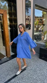 Vestido corto de manga larga con volados, color lavanda, con cuello camisero y botones frontales.