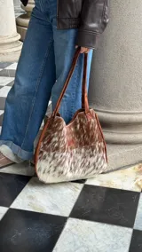 Bolso tipo tote de cuero con pelo de vaca color marrón y blanco. Tiene doble asa de cuero marrón y bolsillo interno.