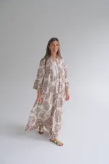 Vestido largo color blanco con estampado floral marrón, cuello mao y mangas 3/4 con volados. Diseño amplio con corte en la cintura y falda escalonada. Cierre frontal con botones.