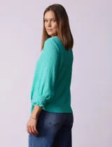 Blusa verde agua de tejido texturado marca Ruby Rd, con cuello a la base, escote en V con aplique metálico, mangas tres cuartos con puños elásticos y terminación de ruedo con nudo.