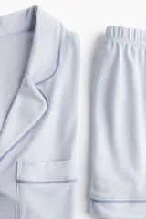 Conjunto de pijama corto celeste con ribetes en azul. Incluye camisa de manga corta con cuello abierto, botones y bolsillo en el pecho, y short con cintura elástica.