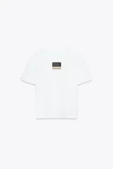Camiseta blanca de manga corta y cuello redondo. Estampado frontal con etiqueta negra y dorada.