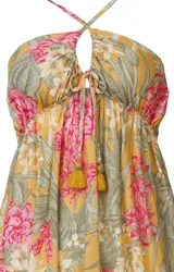 Vestido corto de playa con estampado floral en tonos amarillos, rosas y verdes. Tiene escote halter con tirantes cruzados en la espalda y detalle de borlas amarillas en el frente.