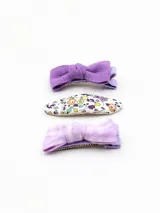 Set de tres broches para el pelo, dos con forma de moño y uno con forma ovalada con estampado floral. Todos en tonos lila y blanco.