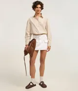 Minifalda cargo color blanco, confeccionada en sarga de algodón, con trabillas, bolsillos laterales y cierre frontal con botón.