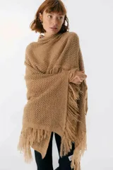 Ruana de punto color beige con cuello alto y flecos.