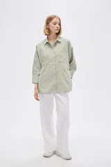Camisa color verde claro, de corte holgado, con cuello clásico, cierre frontal con botones, mangas 3/4 y dos bolsillos de parche en el pecho.