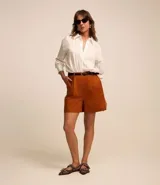 Short de vestir color ladrillo, con cintura alta, trabillas, cierre frontal con botón y cremallera, pliegues delanteros y cinturón de cuero sintético con hebilla metálica.