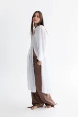 Camisola larga tipo túnica de voile de algodón color blanco, con cuello mao, tablitas a los costados desde el hombro hasta el pecho, manga amplia estilo kimono, lazos a los costados a la altura de la cintura, tajos a los costados y cierre con botones de pasta aplicados en tríos.