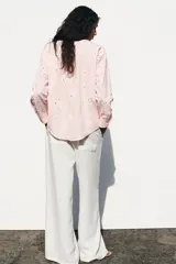 Camisa manga larga color rosa pálido con cuello solapa y cierre frontal con botones. Detalle de bordados perforados engomados con motivos florales. Corte recto.