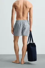 Bañador de hombre confeccionado en tejido técnico con textura. Diseño a rayas verticales en tonos azul y blanco. Cintura elástica ajustable con cordón. Bolsillos laterales y detalle de bolsillo trasero de solapa. Bajo con aberturas laterales. Forro interior.