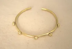 Pulsera rígida de bronce color dorado con bolitas decorativas.