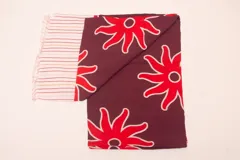 Pareo rectangular de viscosa con estampado de flores rojas sobre fondo borgoña y borde inferior con rayas verticales rojas, amarillas y blancas.