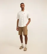 Camisa de hombre de corte relajado, color crudo, con cuello inglés, mangas cortas, abotonado delantero, bolsillo en el pecho y etiqueta de la marca.